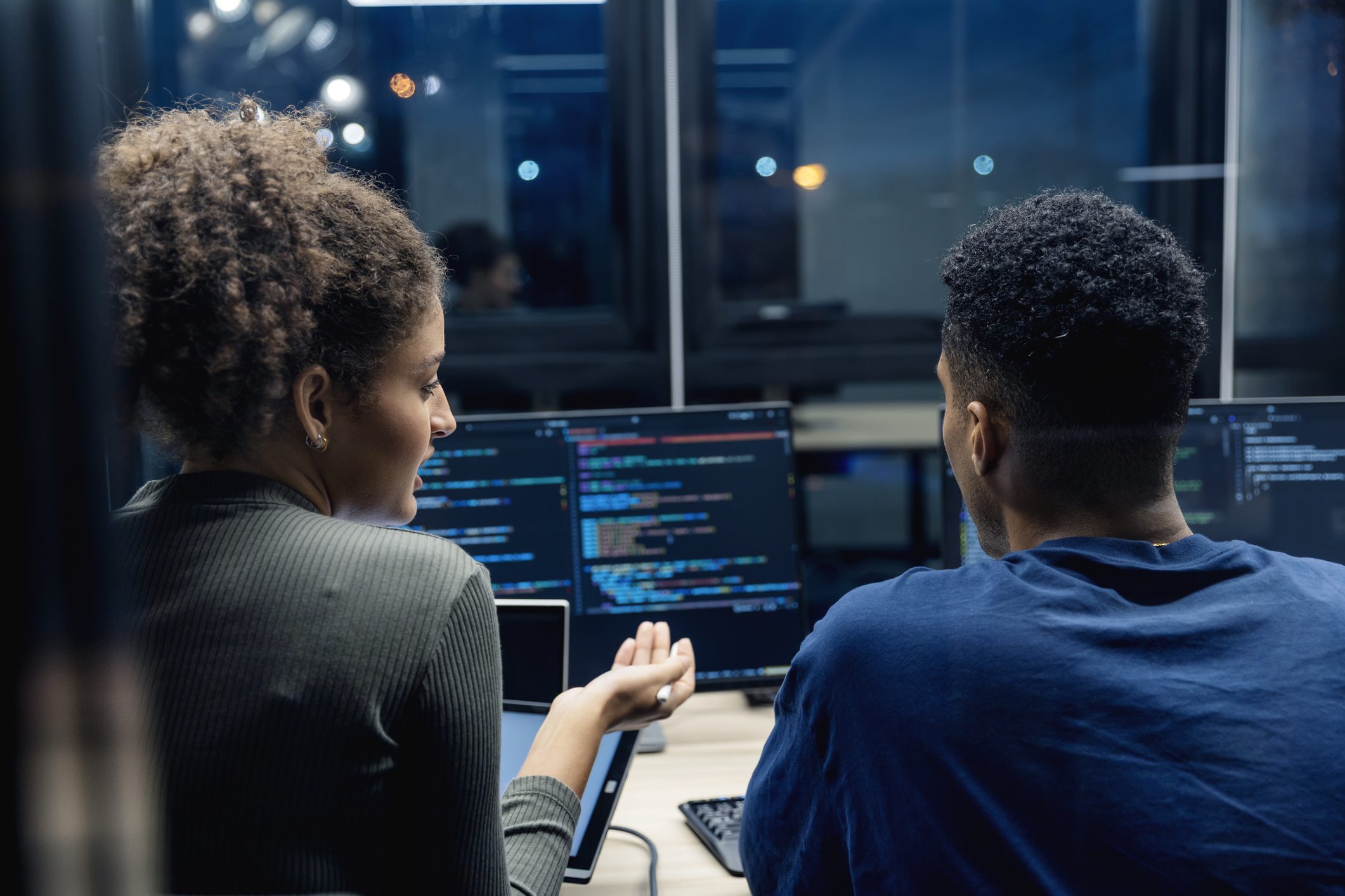 Two developers discussing code on a computer screen in an office.
